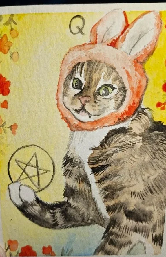 A hand painted tarot card lettered Q, a tabby cat in an orange rabbit hood holding a pentacle, on a yellow ground with red flowers